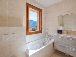 A modern bathroom with a bathtub, a window with a mountain view, and a vanity with a mirror.