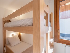 Une chambre avec un lit superposé en bois, une table de chevet et une fenêtre.