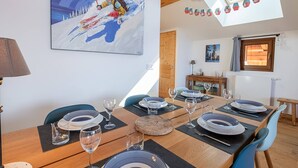 A dining area with a wooden table set for six, surrounded by blue chairs. A large painting of a skier on a snowy mountain is on the wall. - Spacious duplex in Les Saisies for 8 people with parking included (Les Saisies)