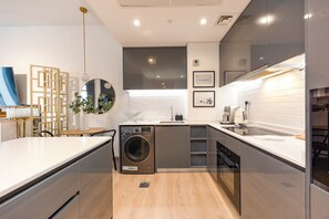 A modern kitchen with a built-in washer and dryer, a wooden dining table, and a kitchen island with a sink. - Bloomfields Stylish 1BR The Bridges  (Abu Dhabi)