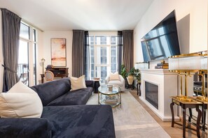 A modern living room with a dark sofa, a glass coffee table, a fireplace, and a large TV mounted on the wall. - Bloomfields Stylish 1BR The Bridges  (Abu Dhabi)