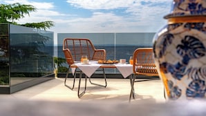 A modern dining area with wicker chairs and a table set for breakfast, overlooking a scenic ocean view.