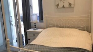 Una camera da letto con un letto in ferro bianco, un comodino con una lampada e una finestra con tende.
