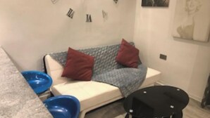Un piccolo angolo living con un divano, due cuscini rossi, una ciotola blu e un tavolino nero.