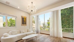 Un salón amplio con un gran ventanal, un sofá blanco, una mesa de centro blanca y una araña.