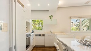 Una cocina moderna con armarios blancos, horno empotrado, lavavajillas y ventana con vistas al verdor.