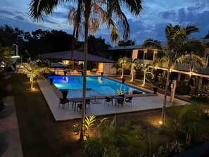 A swimming pool with lounge chairs and tables, surrounded by palm trees and a building with a tiled roof. - Tropical Poolside Apartment - WiFi Aircon Netflix (Dauis)