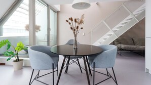 A modern dining area with a round table, two blue chairs, a vase with dried flowers, a potted plant, and a staircase with a white railing. - JULIUS 23: Cozy Stay - 5 Mins to City Center (Wien)