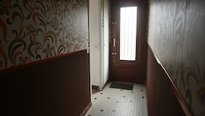 Un pasillo estrecho con papel tapiz estampado, una puerta de madera y suelo de baldosas.