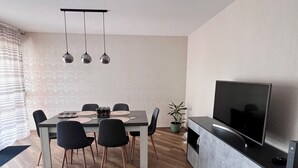 Een moderne woonkamer met een eethoek, voorzien van een flatscreen televisie, een eettafel met stoelen en een potplant.