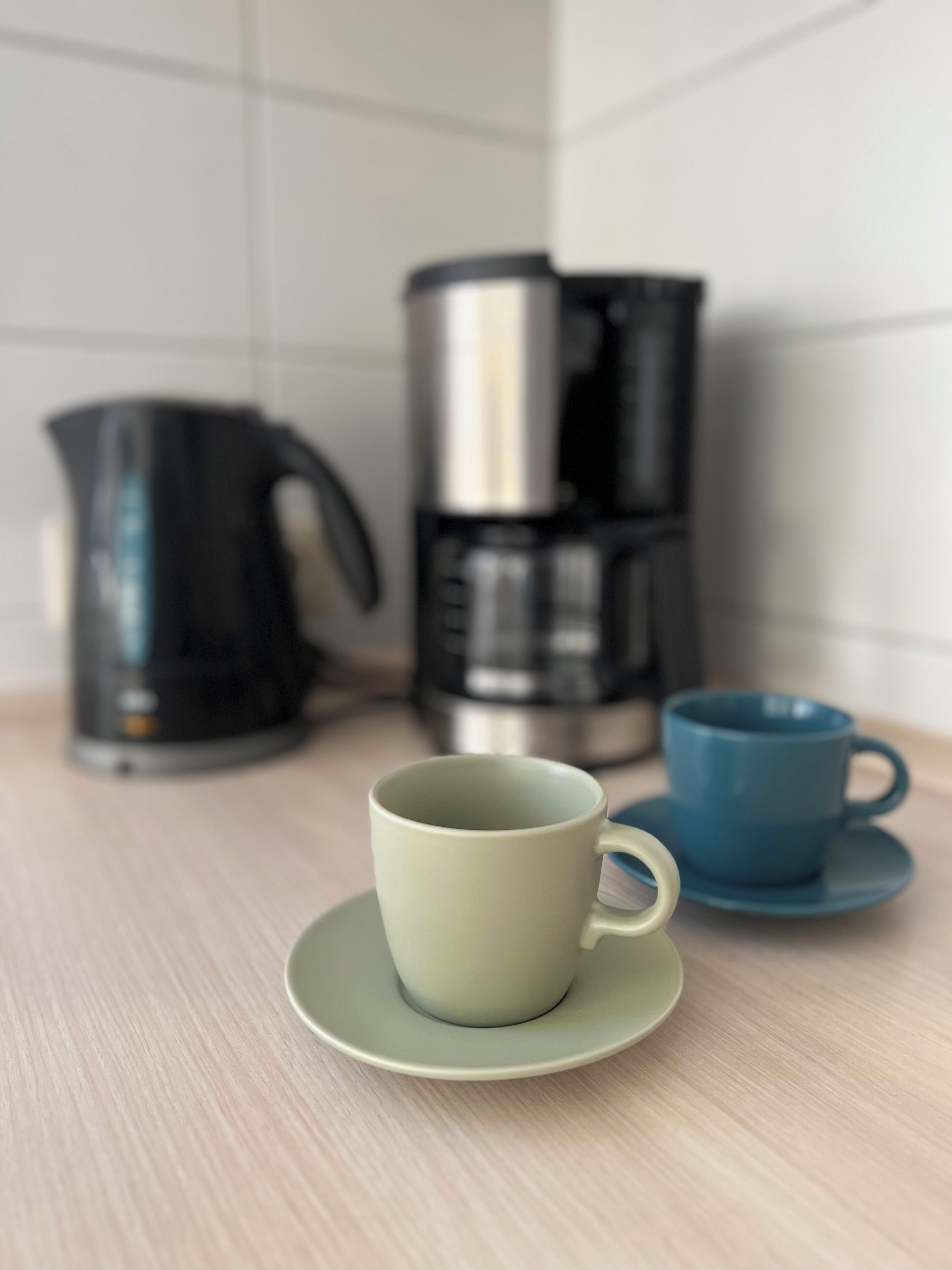 Un piano di lavoro in cucina con una tazza verde su un piattino, una tazza blu su un piattino e due macchine da caffè.