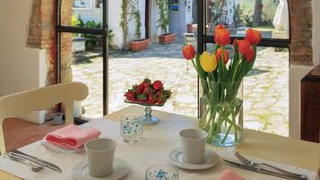 Una mesa de comedor con vista a un patio a través de un ventanal arqueado, un jarrón de tulipanes y un bol de fresas.