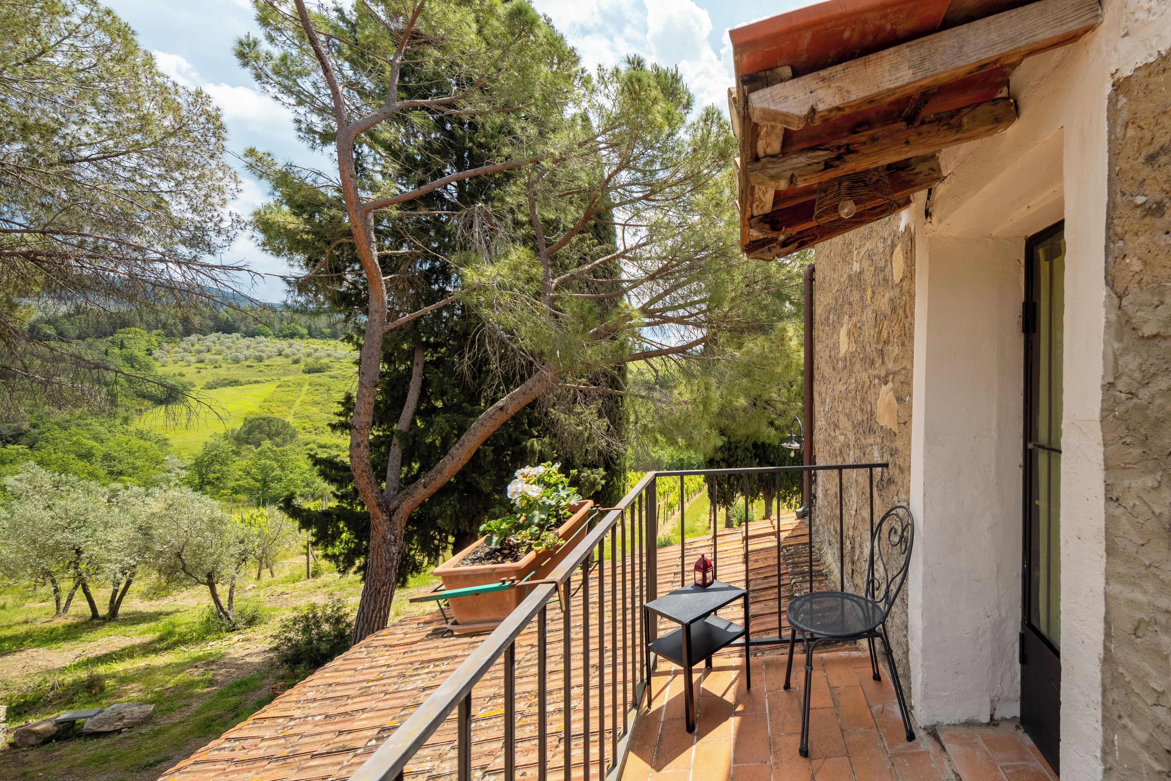Un balcón con vistas a un paisaje verde, una planta en maceta y una silla de metal.