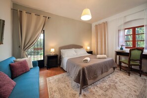 Une chambre à coucher comprenant un lit, des tables de chevet, un bureau, une chaise, un canapé et une fenêtre avec des rideaux.