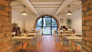 Un comedor con paredes de ladrillo, vigas de madera y un amplio ventanal de arco que da a un patio.