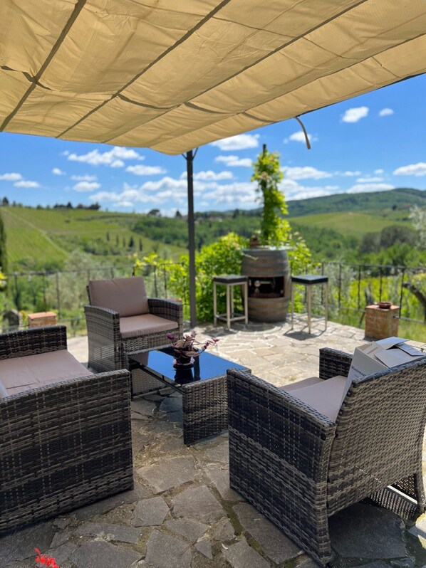 Une terrasse extérieure aménagée avec des meubles en osier, une table et une vue sur des collines verdoyantes.