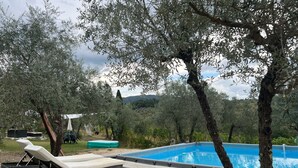 Una piscina rodeada de olivos, con sillas de descanso y una pequeña mesa cerca.