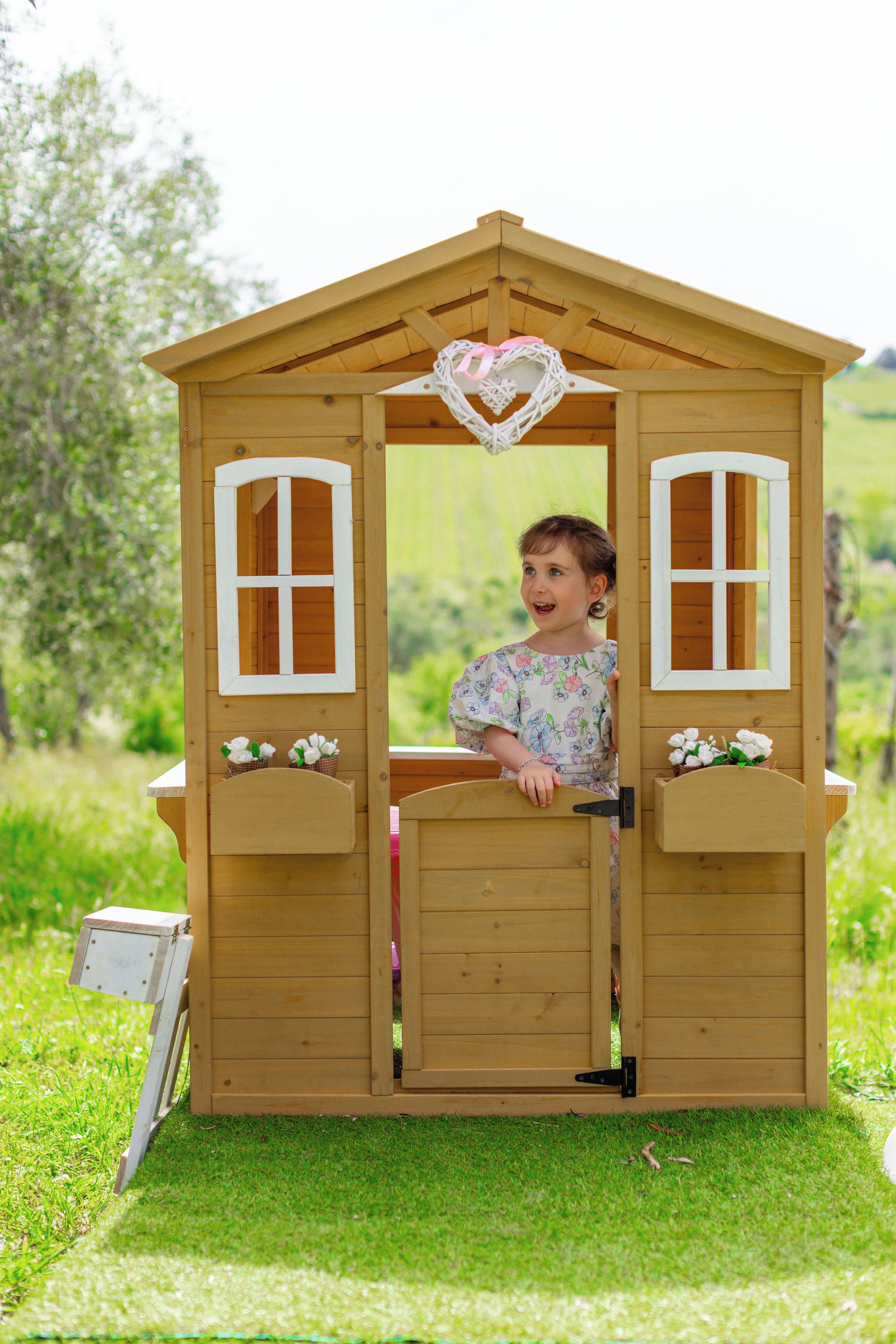 A wooden playhouse with two windows and a heart-shaped decoration on the roof.