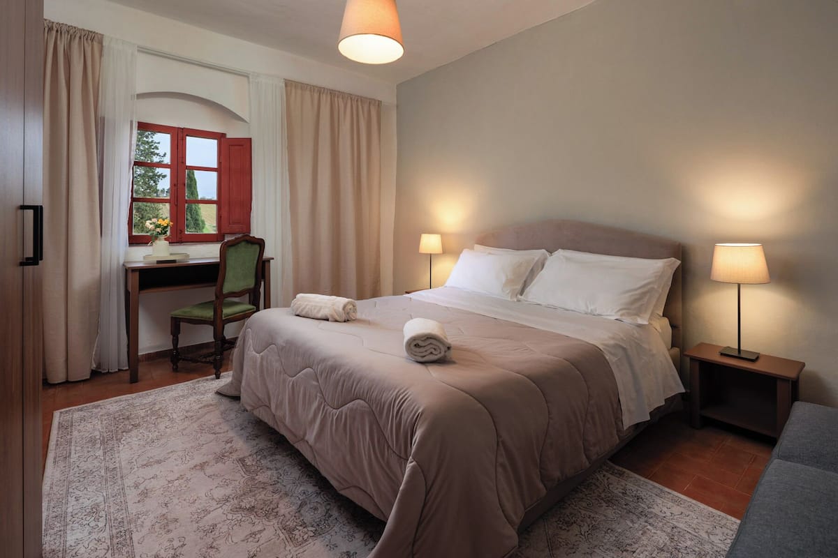 Un dormitorio ordenado con cama, lámparas de noche, escritorio y silla.