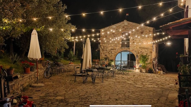Un patio al aire libre con suelo de piedra, mesas, sillas, luces colgantes y plantas en macetas.
