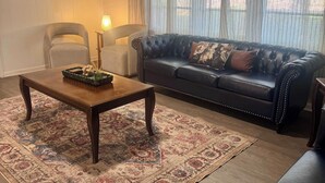 Olohuoneessa on tumma nahkasohva, puinen sohvapöytä ja kuviollinen matto.