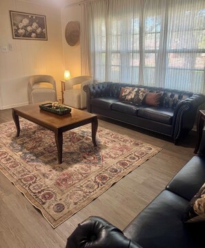 A living room with a dark leather sofa, a wooden coffee table, and a patterned rug. - Ivy Lodge (Sleeps 8 | 5 Tvs) (Abilene)
