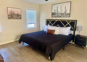 Een slaapkamer met een bed, een nachtkastje, een lamp en twee foto's aan de muur.