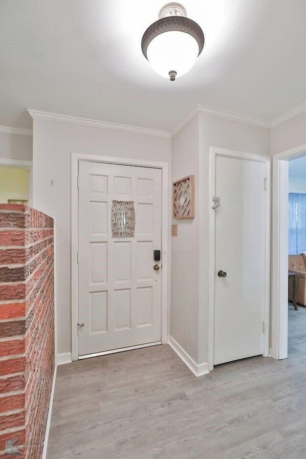 A hallway with a white door, a brick wall, and a ceiling light fixture.