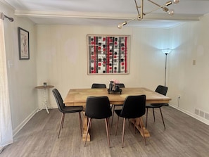 Een eetgedeelte met een houten tafel, zwarte stoelen en een decoratieve wandversiering.