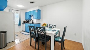 Een kleine keuken met blauwe kastjes en een eethoek met een tafel en stoelen.