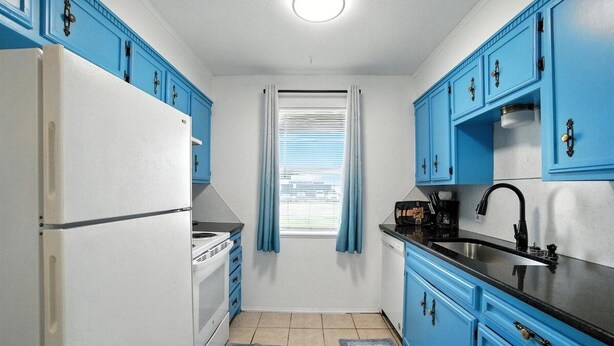 Een kleine keuken met blauwe kastjes, een witte koelkast, een fornuis en een spoelbak.