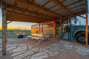 A bus converted into a stationary structure with a covered area, picnic table, and outdoor seating.