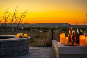 A stone hot tub with candles and bottles, overlooking a landscape with hills during sunset. - Oasis Pool- Schoolie | Heated Pool and Hot Tub! (Abilene)