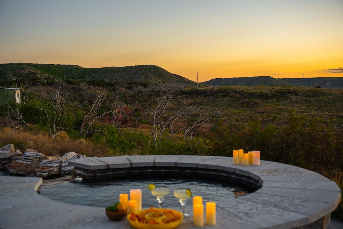 Ein Whirlpool mit Kerzen und einer Schüssel Essen, eingebettet in eine natürliche Landschaft.