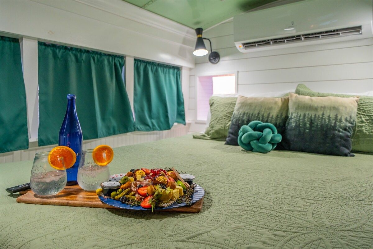 Een kamer met een bed, een houten nachtkastje met een fruitschaal en glazen, en een blauwe fles.
