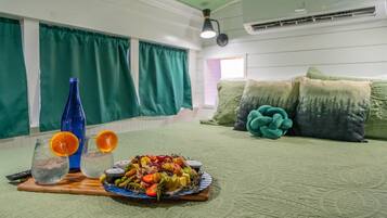 Een kamer met een bed, een houten nachtkastje met een fruitschaal en glazen, en een blauwe fles.