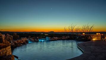 A nighttime view of a swimming pool with a waterfall feature, surrounded by rocks and a clear sky.