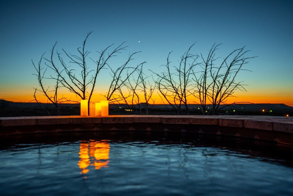 A sunset over a body of water with bare trees silhouetted against the sky.