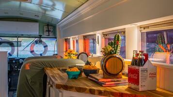 A cozy interior with a wooden bar area, a bar stool, a bucket of snacks, a wooden barrel, and a Coca-Cola cooler.