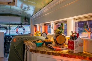 A cozy interior with a wooden bar area, a bar stool, a bucket of snacks, a wooden barrel, and a Coca-Cola cooler.