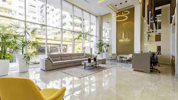 Un hall d’hôtel moderne doté d’un grand espace salon, d’un comptoir d’accueil et de grandes fenêtres offrant une vue sur les bâtiments environnants.