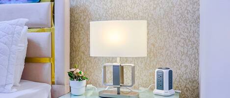 A neatly arranged hotel room with a bed, bedside table, lamp, and a small potted plant.