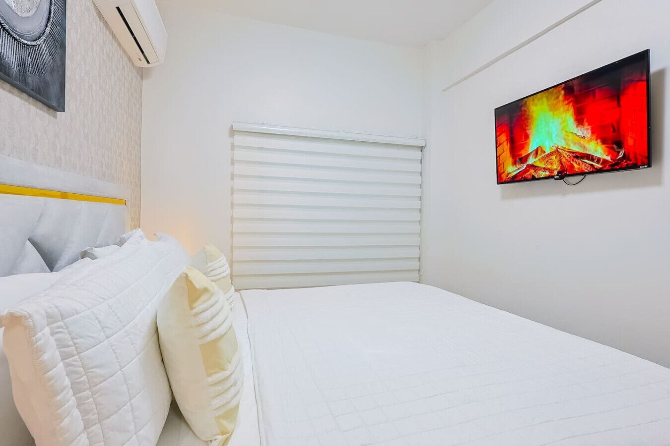 Een hotelkamer met een bed, wit beddengoed, een schilderij van een vuur en een raam met jaloezieën.