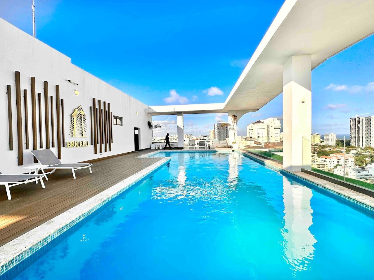 Una piscina en la azotea con vistas al horizonte de la ciudad, una pared blanca con listones de madera verticales y la palabra "BRICKELL" en la pared.
