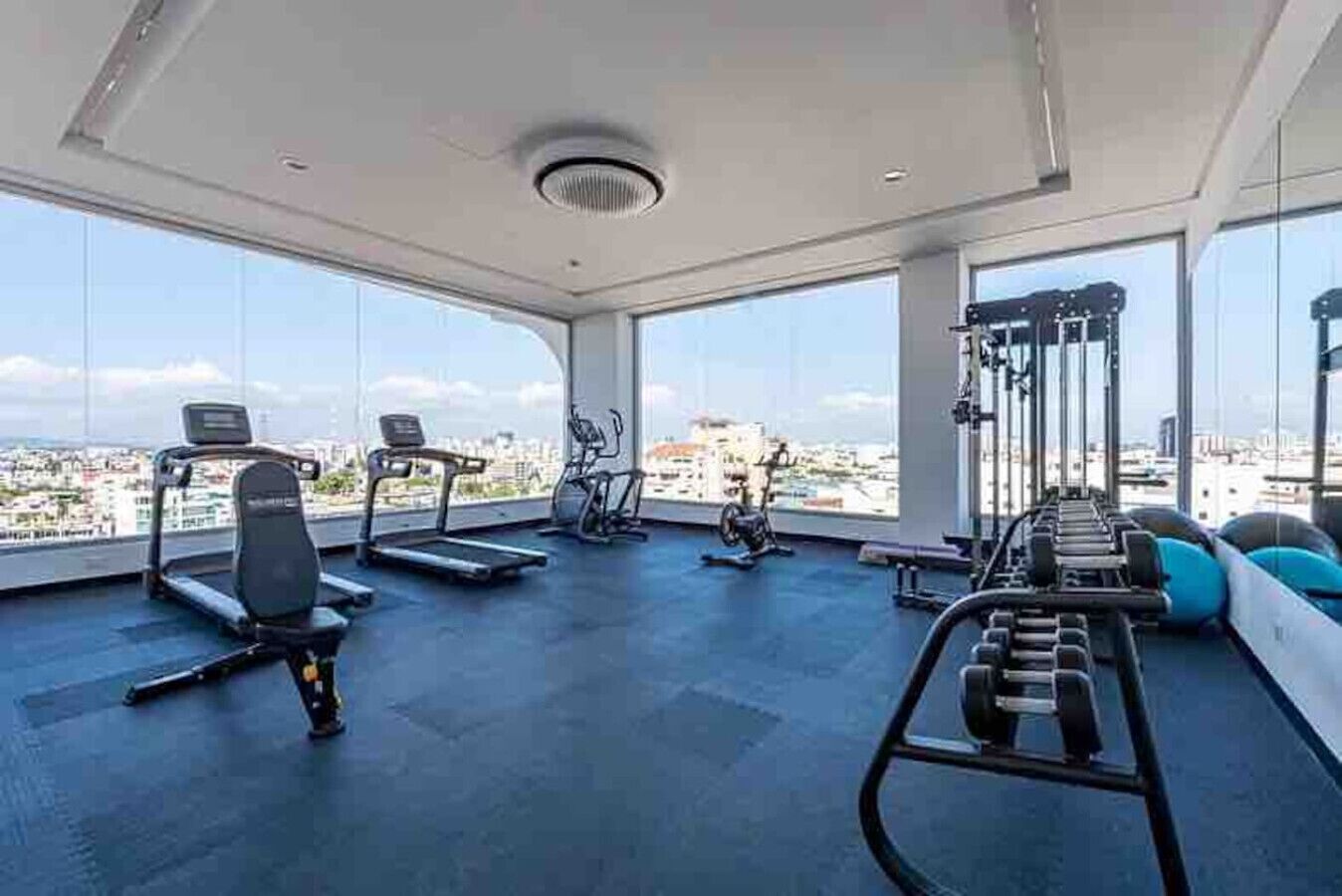 Ein Fitnessstudio mit Laufbändern, Ergometer und Krafttrainingsgeräten, große Fenster mit Blick auf die Stadt.