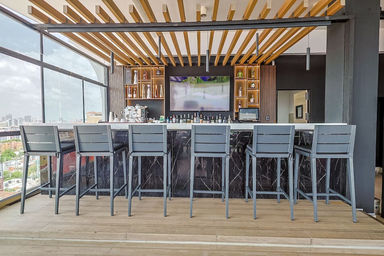 Un bar situé sur le toit, doté d’un design moderne, avec un comptoir en marbre, de nombreux tabourets et un grand écran de télévision.