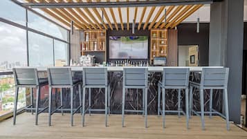 Un bar situé sur le toit, doté d’un design moderne, avec un comptoir en marbre, de nombreux tabourets et un grand écran de télévision.