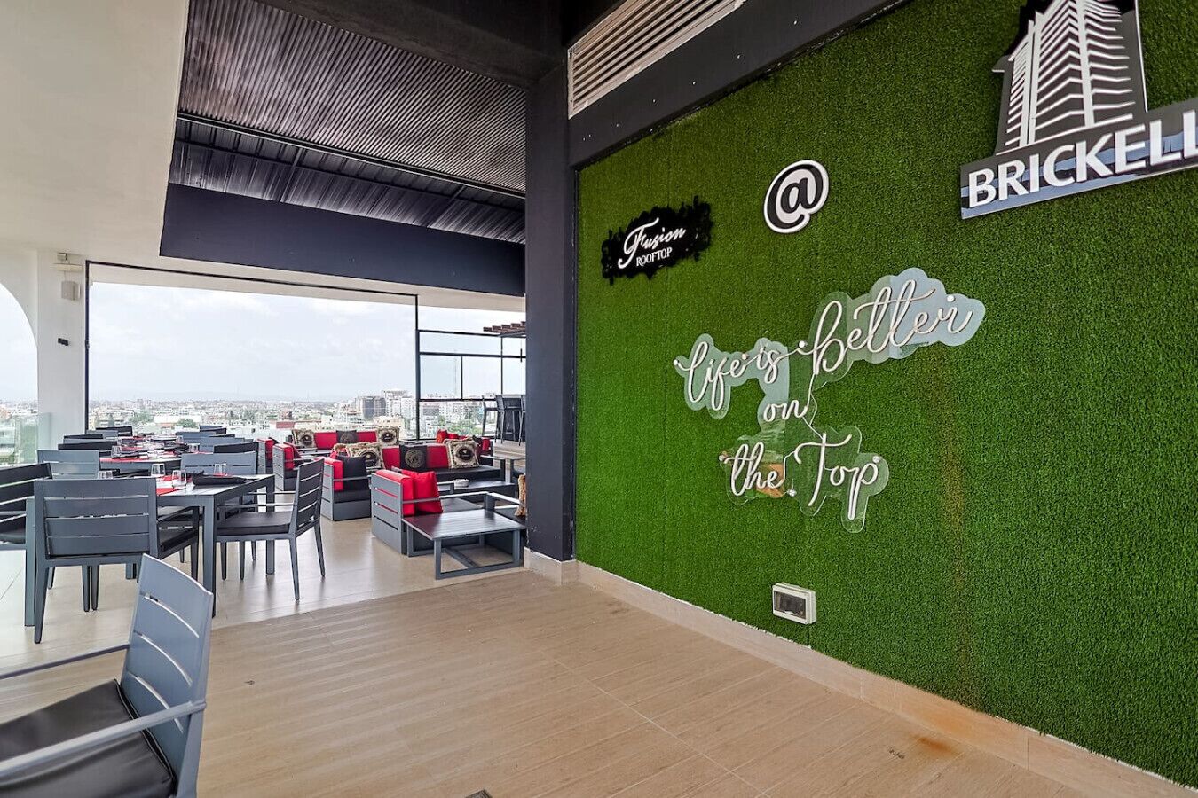Ein Restaurant im Obergeschoss mit Blick auf die Stadt, eine grüne Wand mit Text und ein Schild mit der Aufschrift 'Brickell'.
