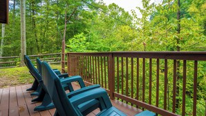 Une terrasse en bois avec des chaises bleues et une balustrade donnant sur une zone boisée.