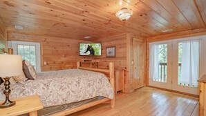 A wooden cabin bedroom with a bed, a television, and a window.